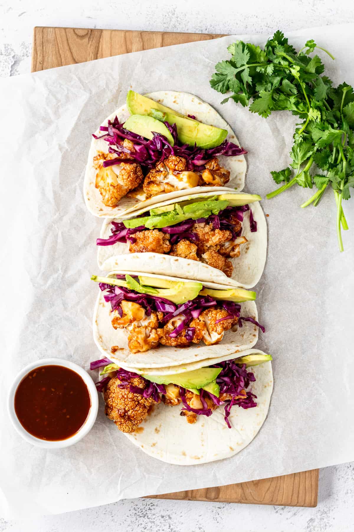 Four BBQ cauliflower tacos on a serving platter with sauce and cilantro. 