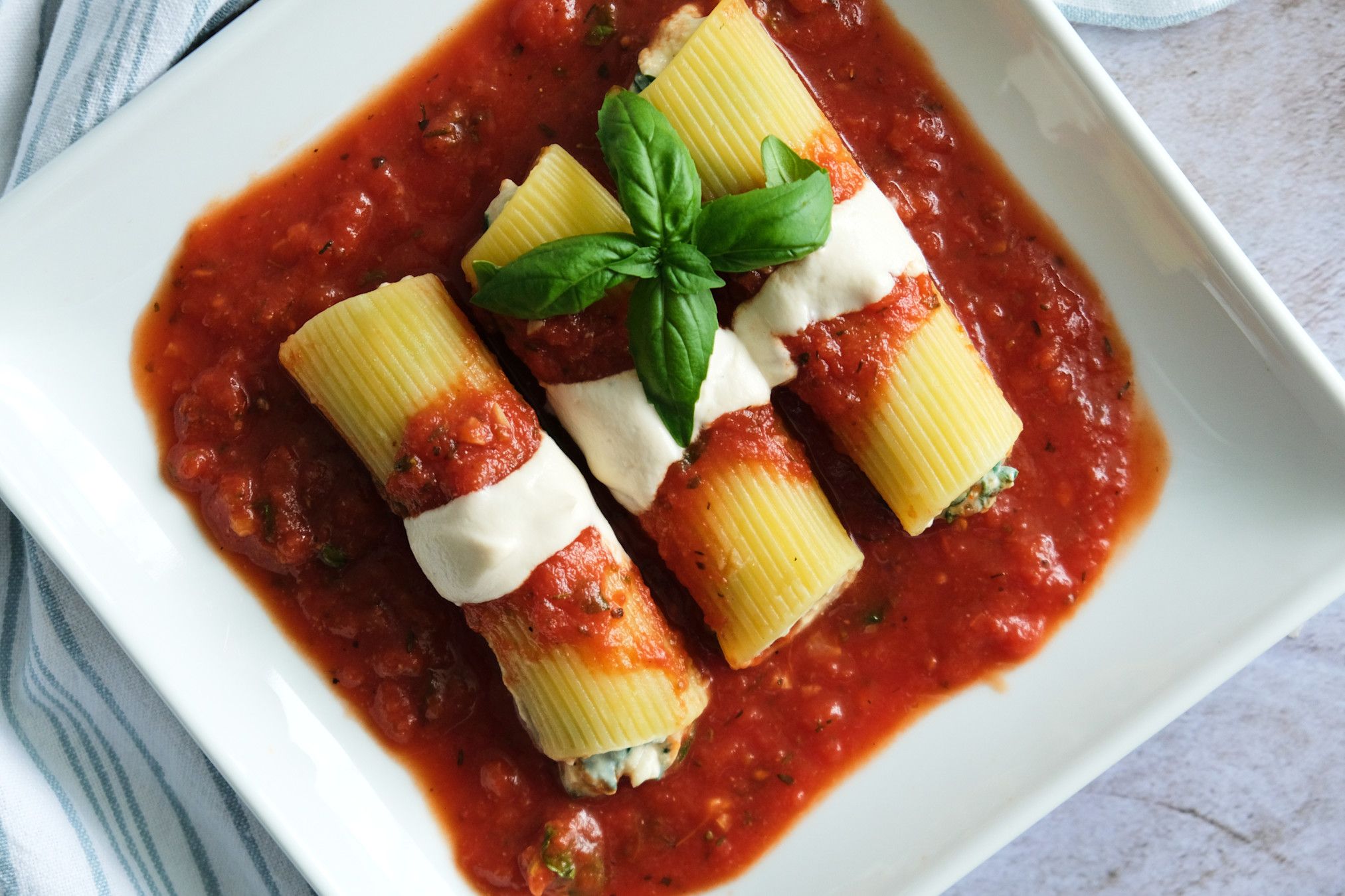 A top-down view of three vegan cannelloni on a square plate.