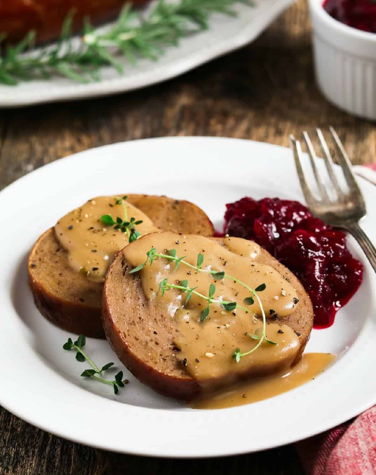 Vegan holiday roast slices on a plate with gravy and cranberry sauce.