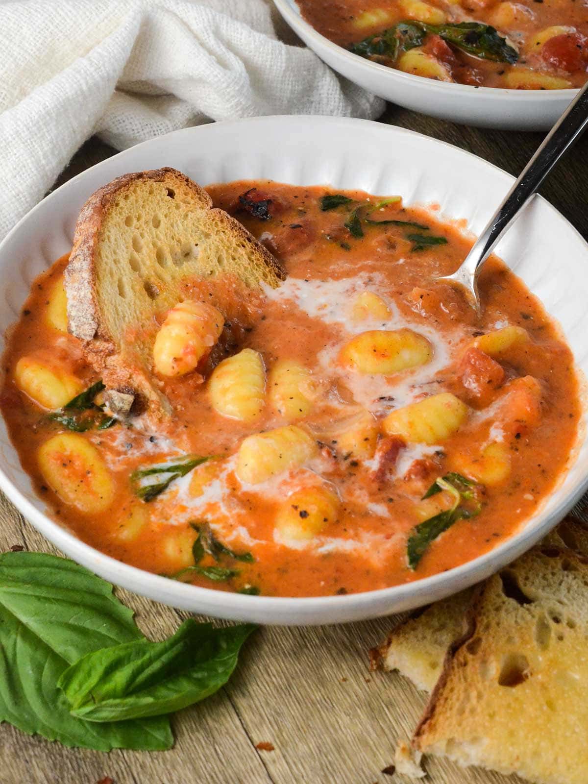 A bowl of tomato gnocchi soup with a piece of bread dipped in.