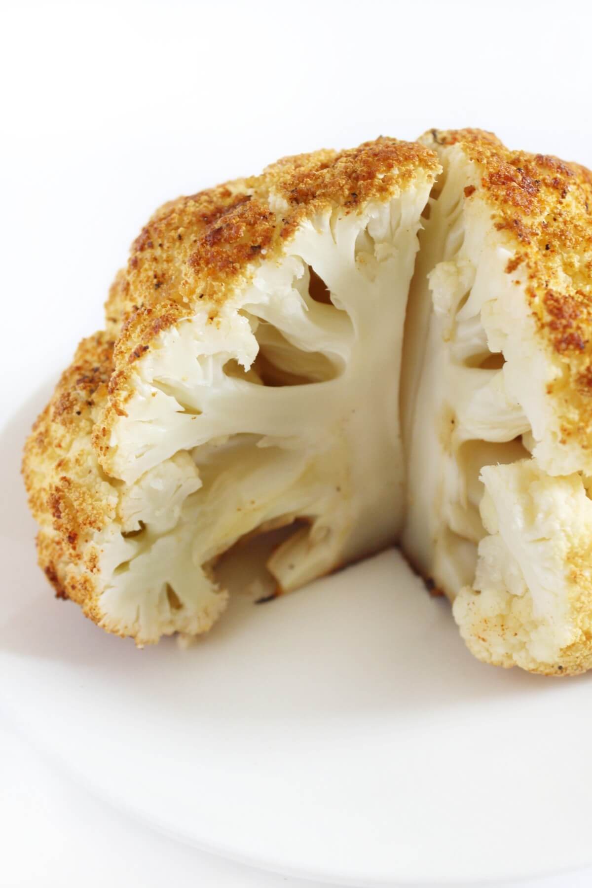 Whole roasted cauliflower on a plate, with a quarter sliced out. 