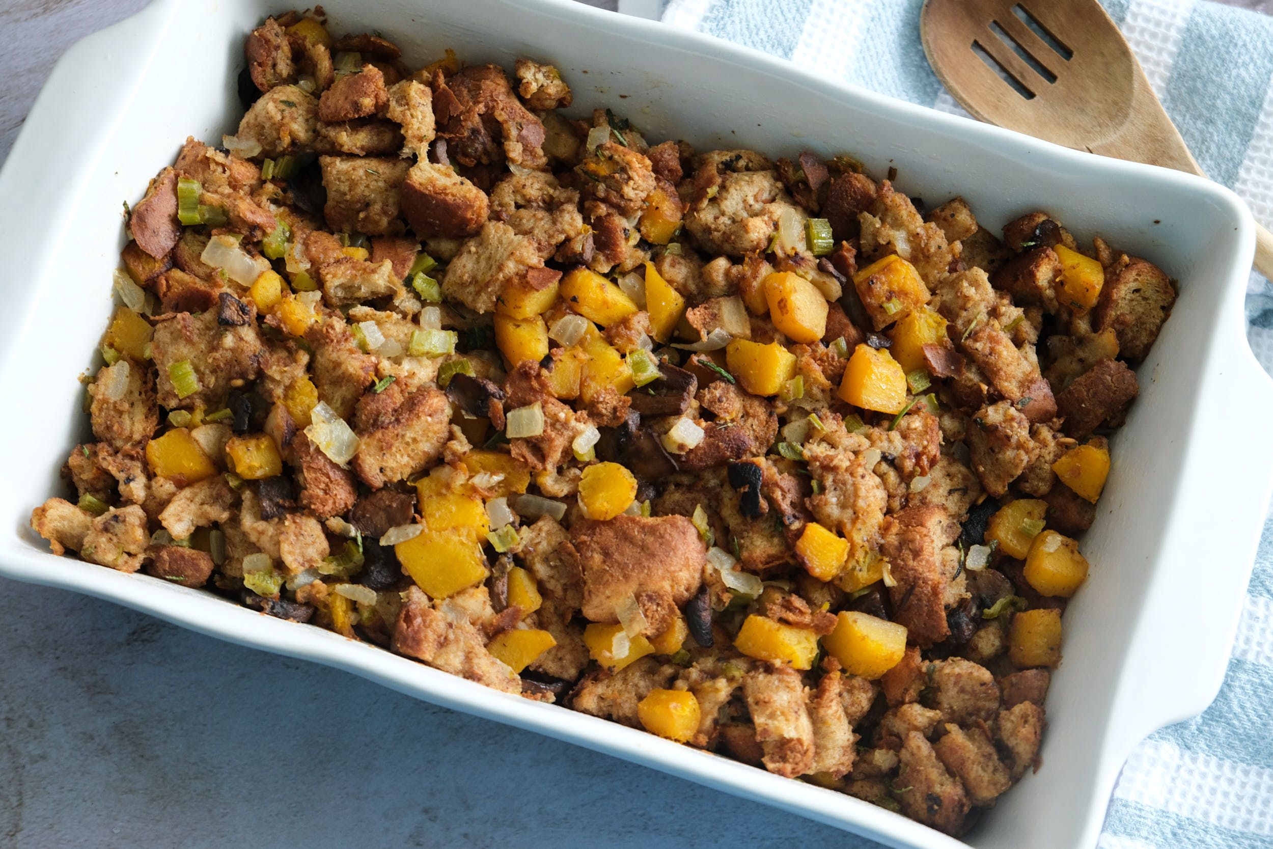 top down view of butternut squash stuffing in casserole dish with a wooden spoon on the side