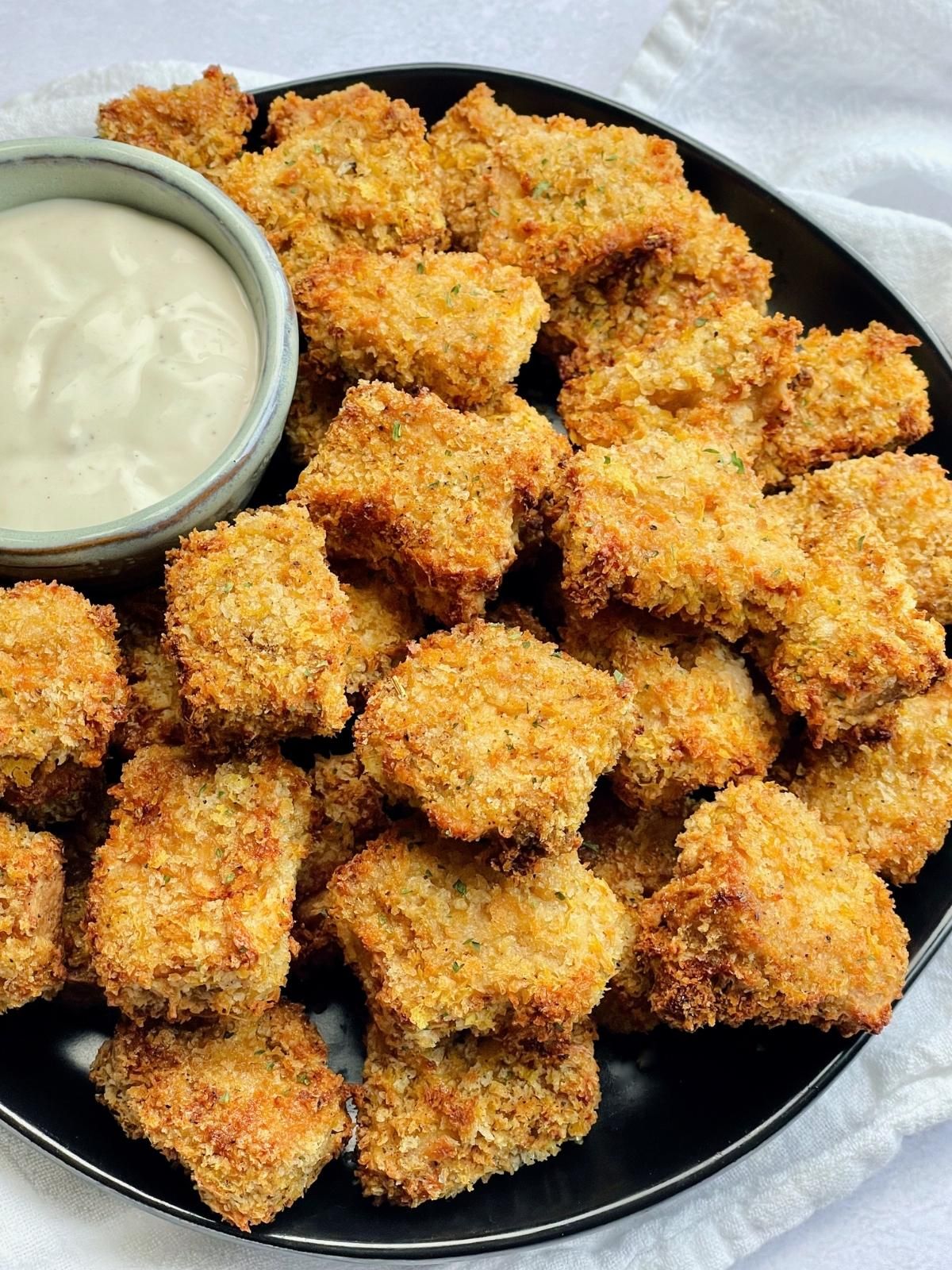 A large platter of tofu nuggets with a small bowl of dipping sauce. 