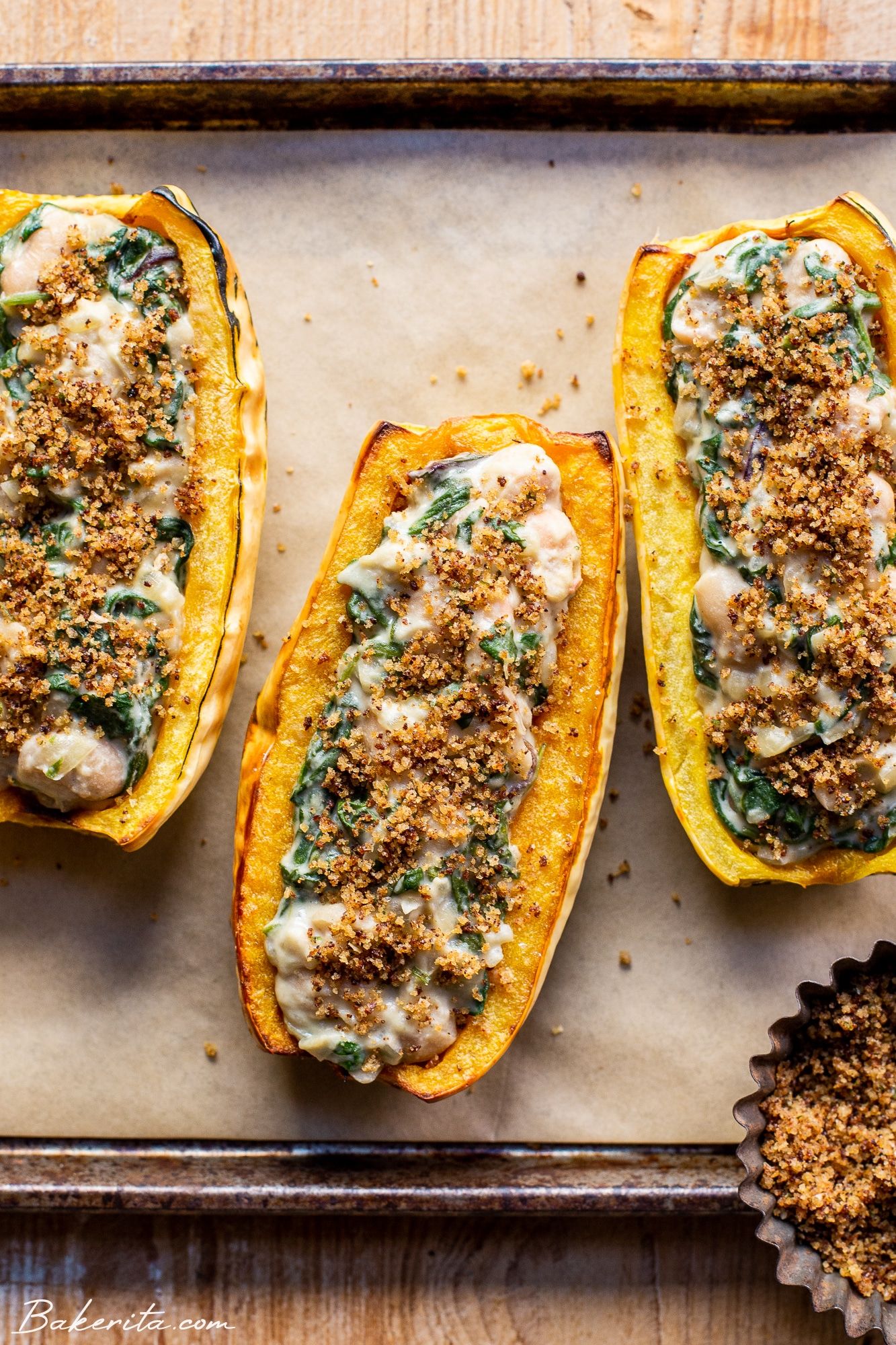 Stuffed delicata squash halves on a parchment-lined baking tray.