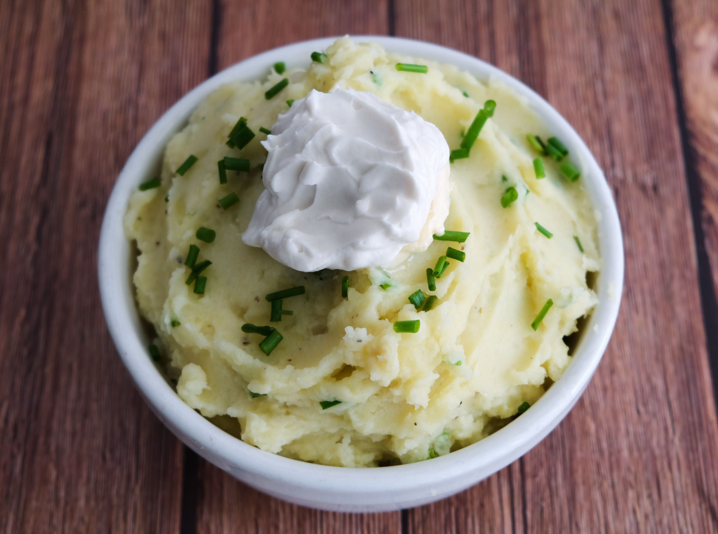A bowl of vegan sour cream mashed potatoes with chives and sour cream on top