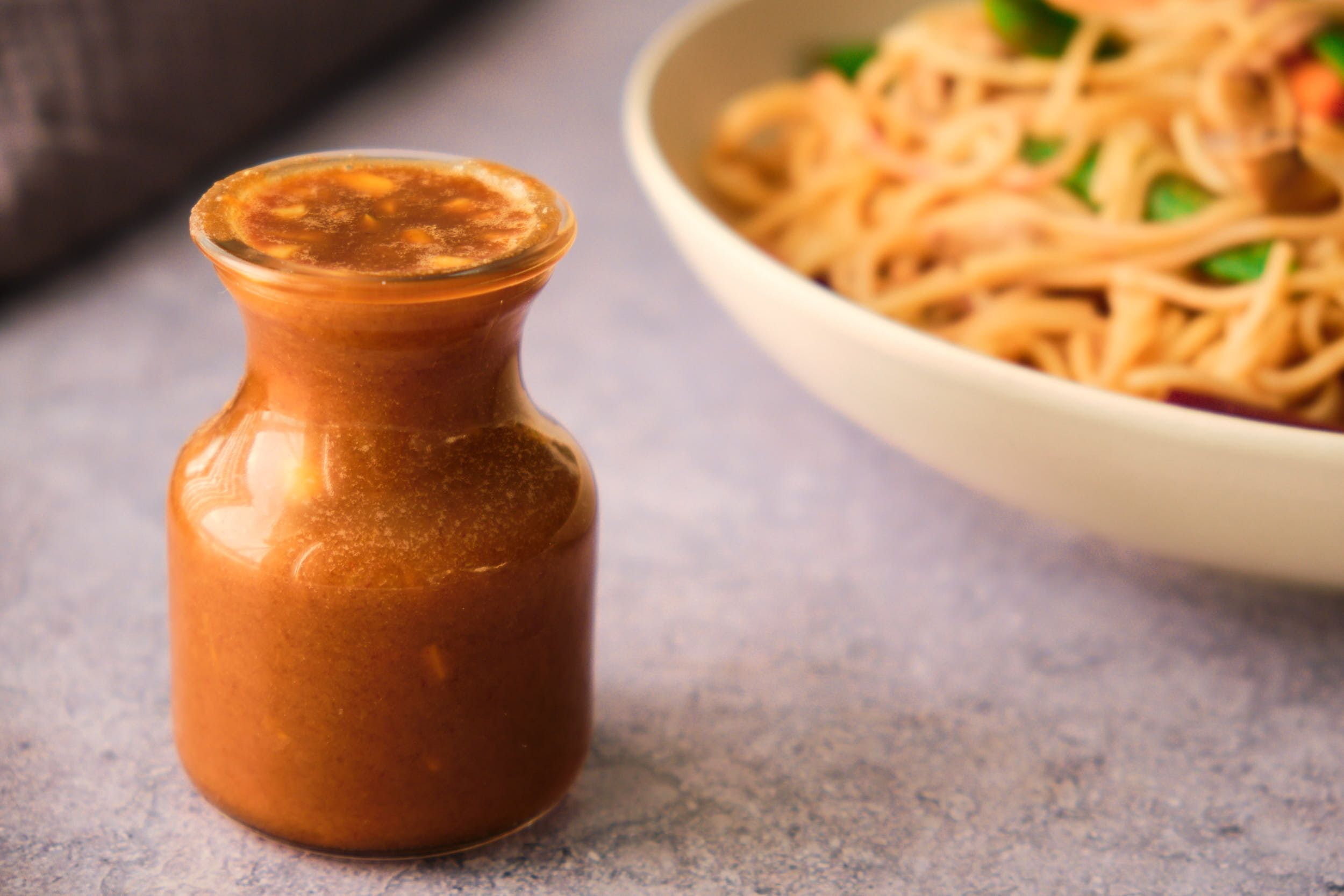 A jar of peanut sauce with a bowl of noodles in the background