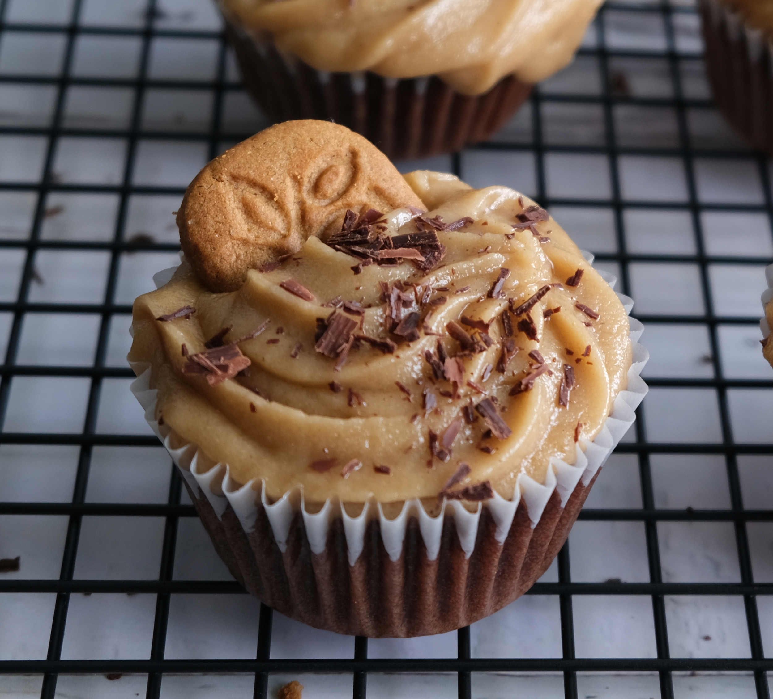 A closeup of a chocolate cupcake with cookie butter frosting, topped with shaved chocolate and a speculoos cookie