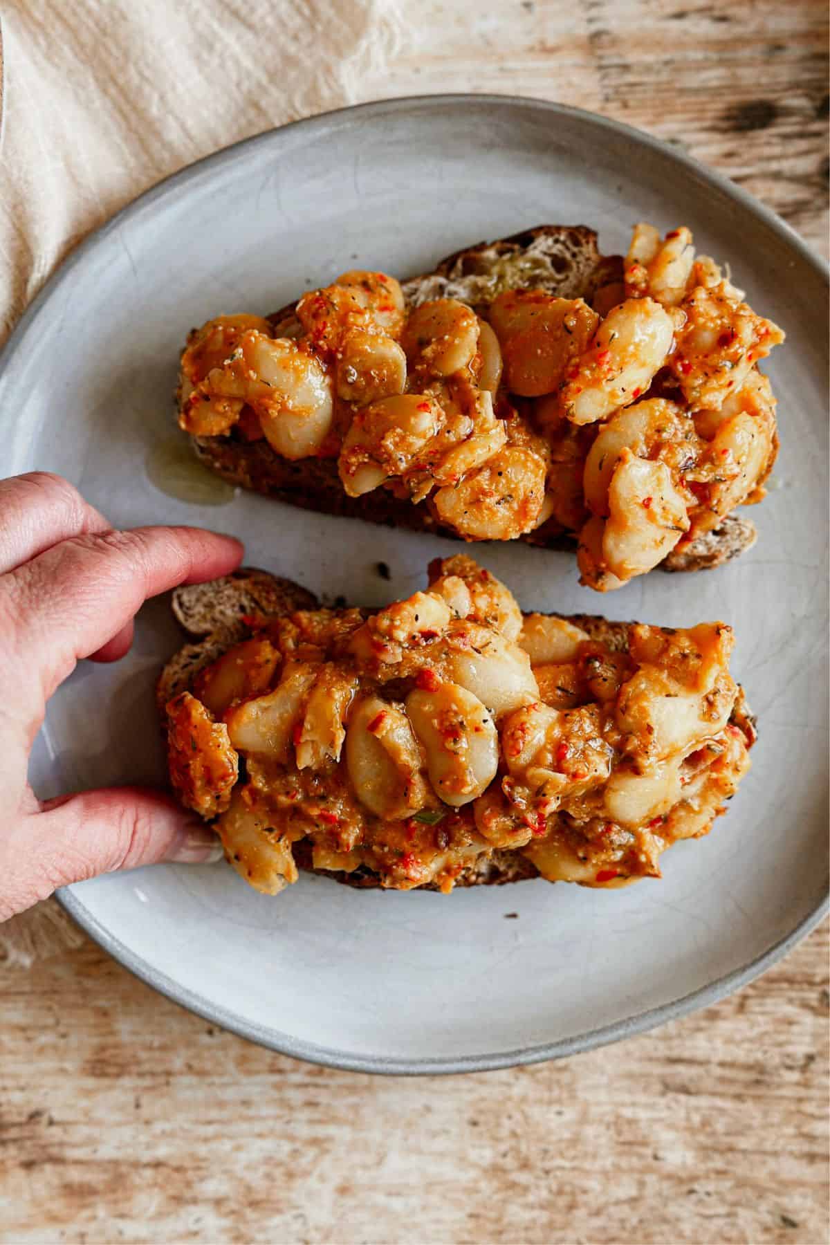 A hand taking one piece of a spicy miso butter bean open-faced sandwich from a plate. 