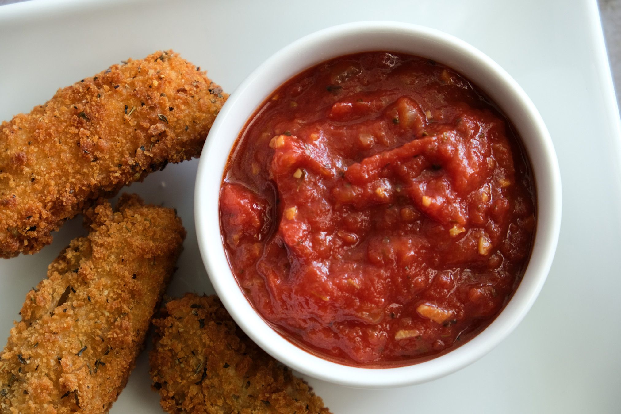 spicy marinara sauce in ramekin with mozzarella sticks on side