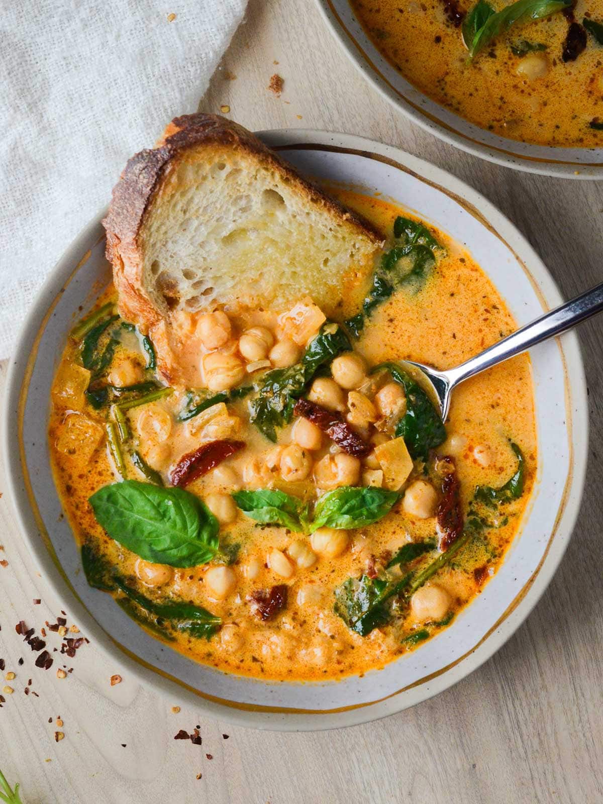 A bowl of Tuscan chickpea soup with a slice of bread dunked in it.