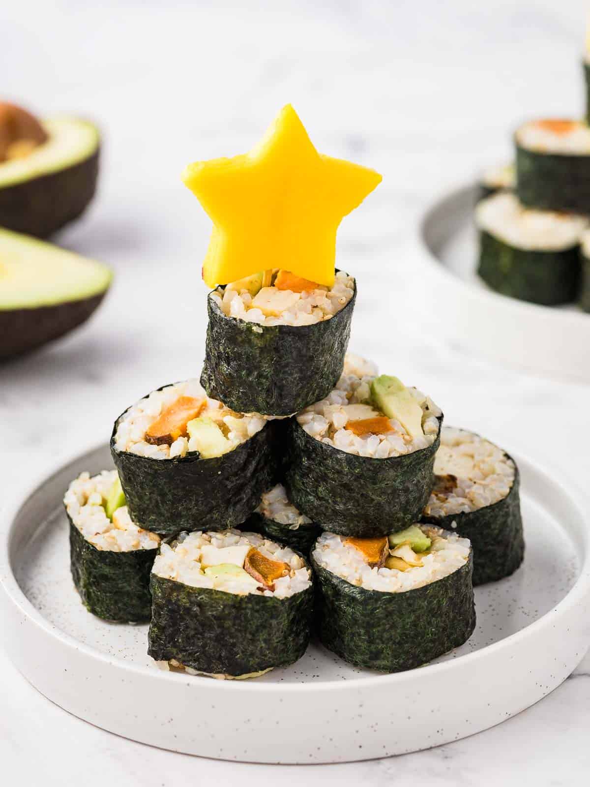 Vegan sushi rolls stacked in a Christmas tree arrangement, with a star cut from a mango on top. 