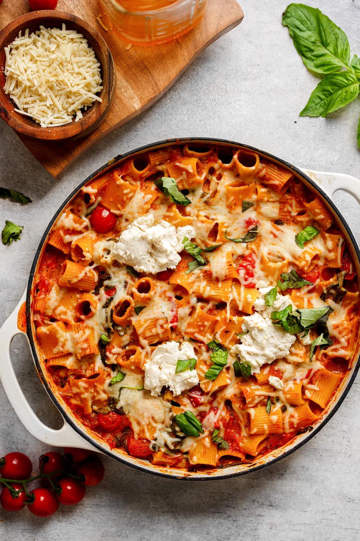 A top-down view of a pot of vegan pasta bake topped with basil and vegan cheeses. 
