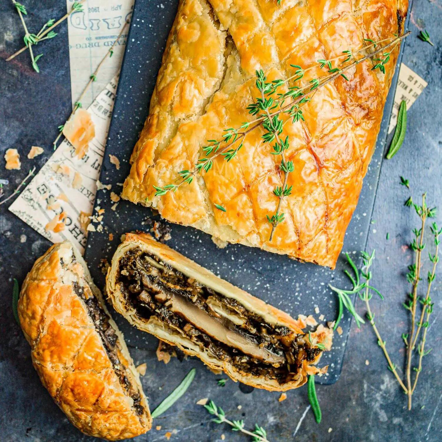 Vegan mushroom wellington, sliced, on a table with thyme sprigs.