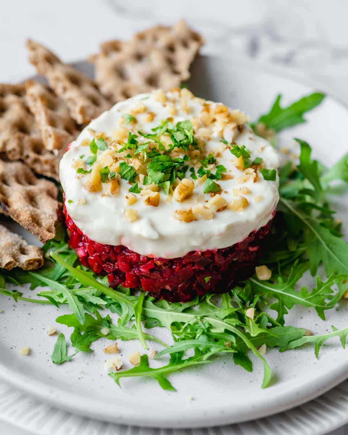 Vegan beetroot tartare on arugula leaves with crackers in the background. 