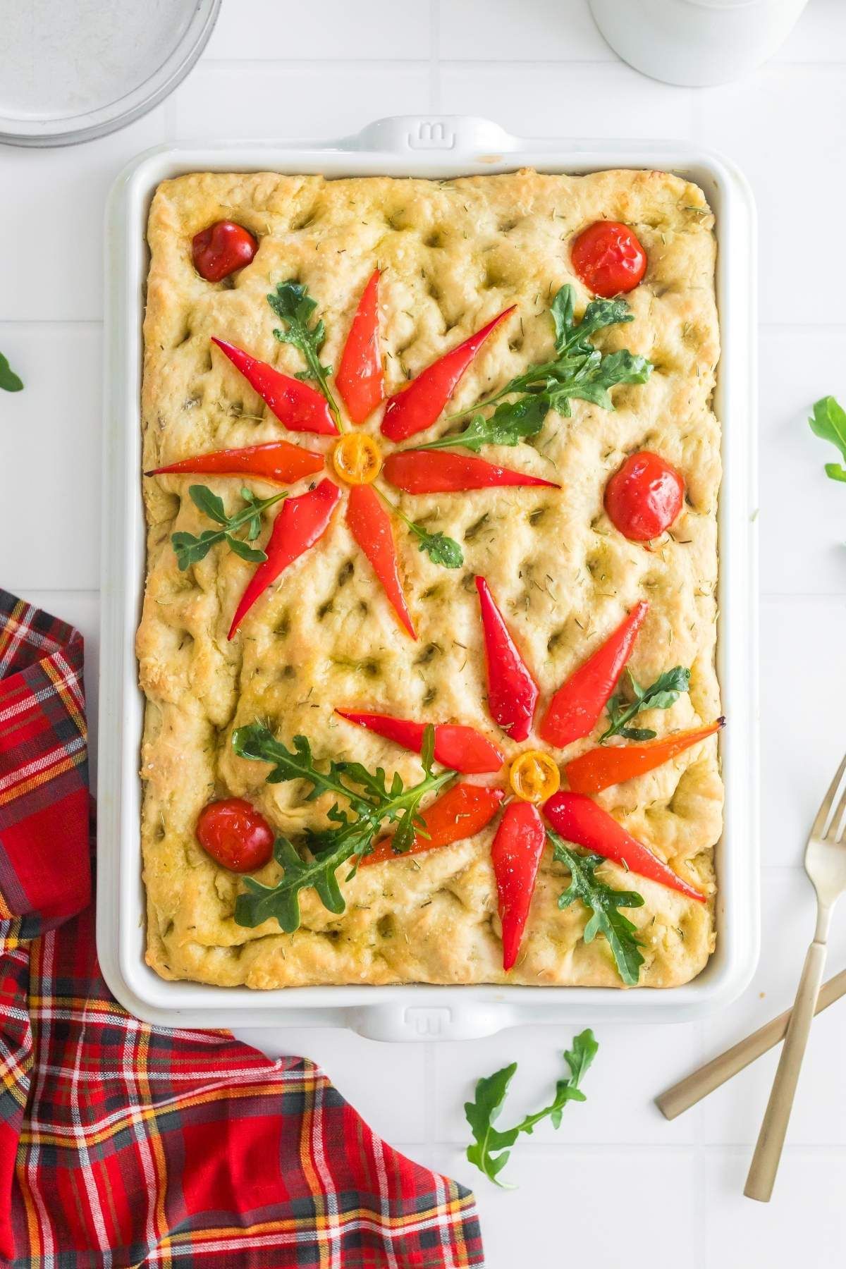 Christmas focaccia on a table with a poinsettia design next to a red plaid linen and forks. 