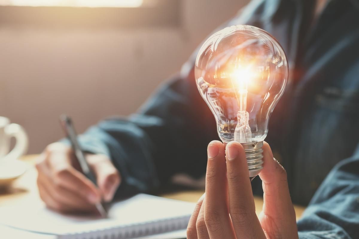 Man holding a lightbulb while working on laptop