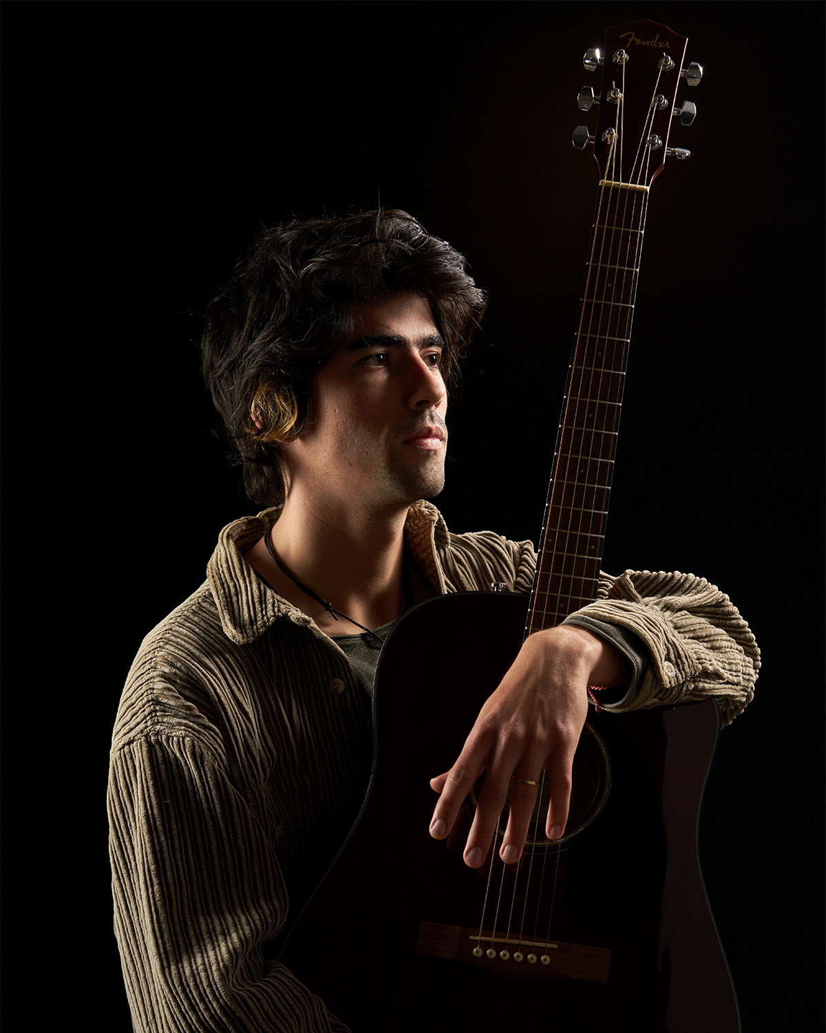 A musician resting on an acoustic guitar in low warm light