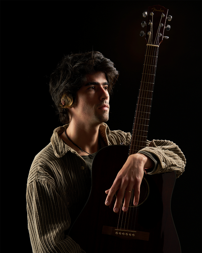 A musician resting on an acoustic guitar in low warm light