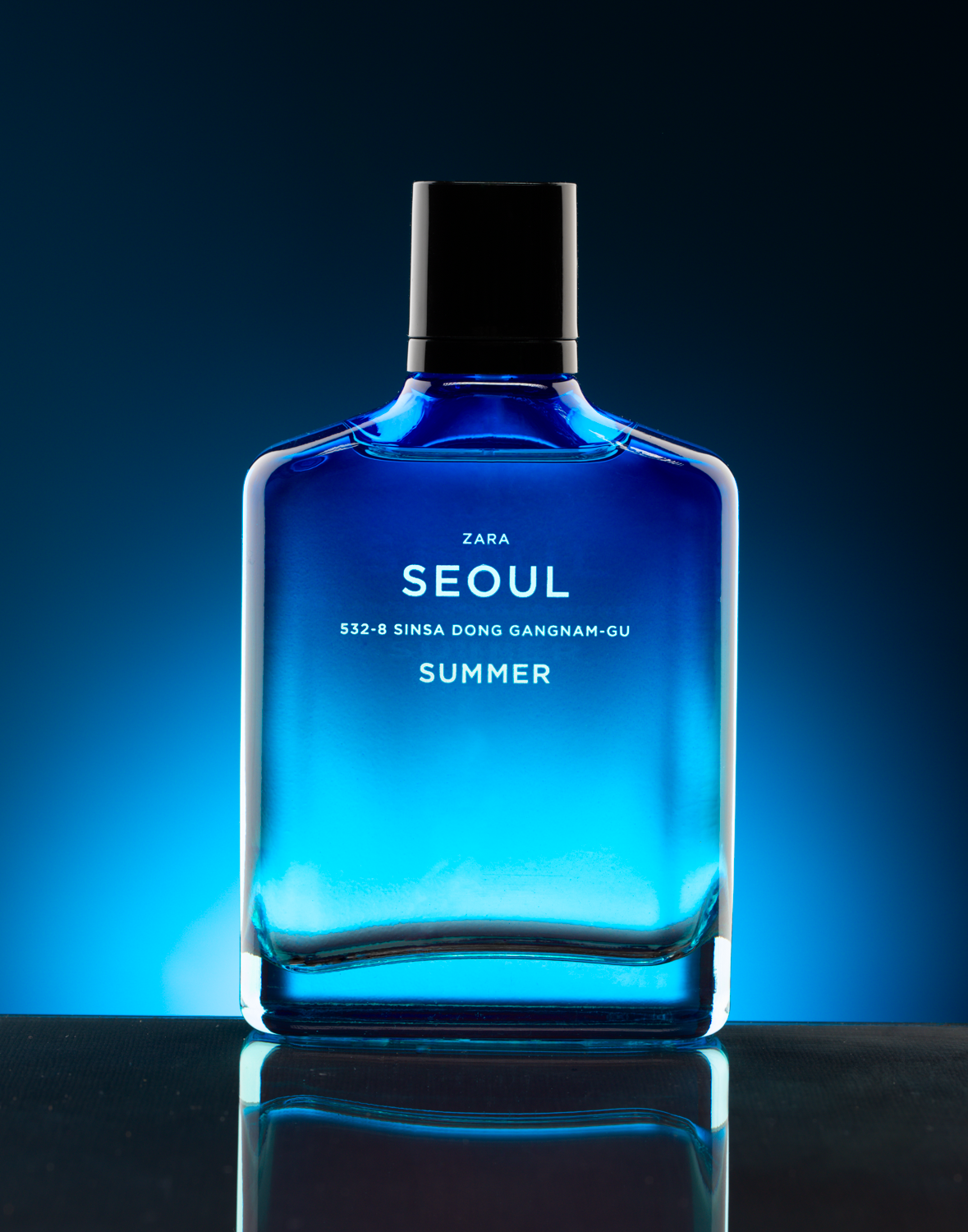 A blue glass fragrance bottle lit against a dark reflective surface