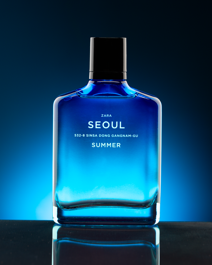 A blue glass fragrance bottle lit against a dark reflective surface