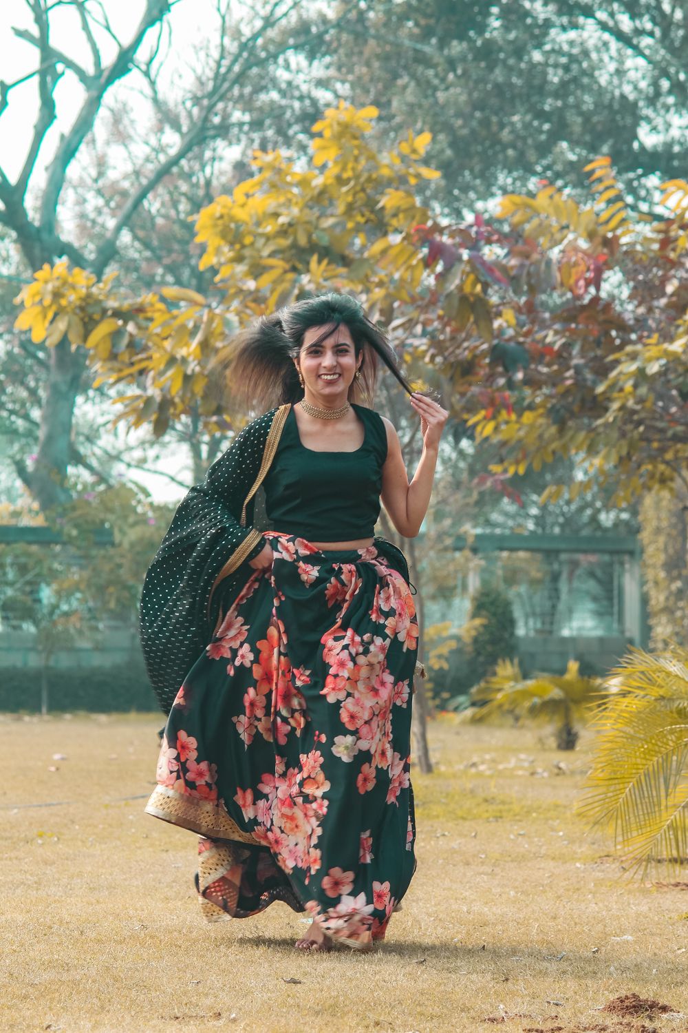 A woman in a floral lehenga turning mid-step in a sunlit park