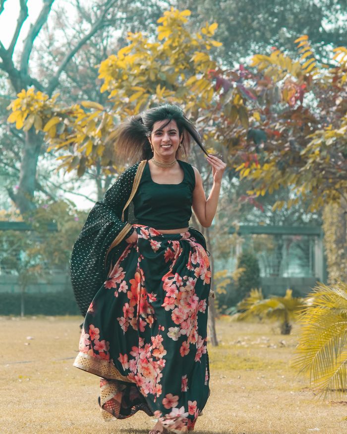 A woman in a floral lehenga turning mid-step in a sunlit park