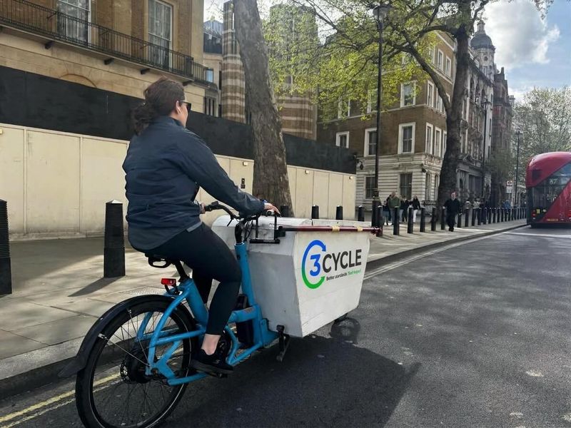 3Cycle operative riding an electric cargo bike through central London, with a red double-decker bus behind