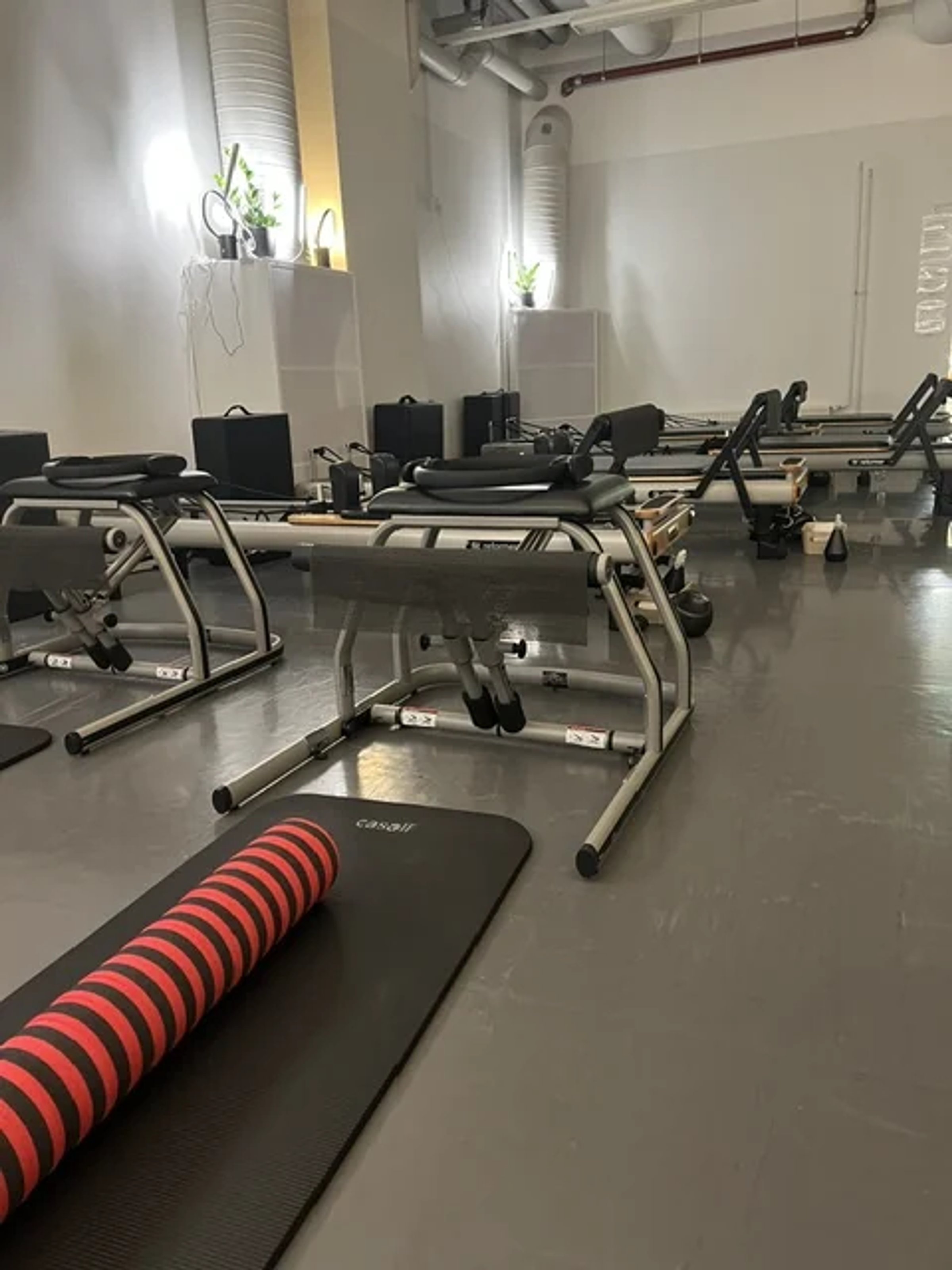 Punainen pilatesrulla ja matto, taustalla Reformer-laitteet Pilates Ateljén salissa