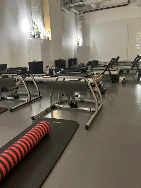 Punainen pilatesrulla ja matto, taustalla Reformer-laitteet Pilates Ateljén salissa