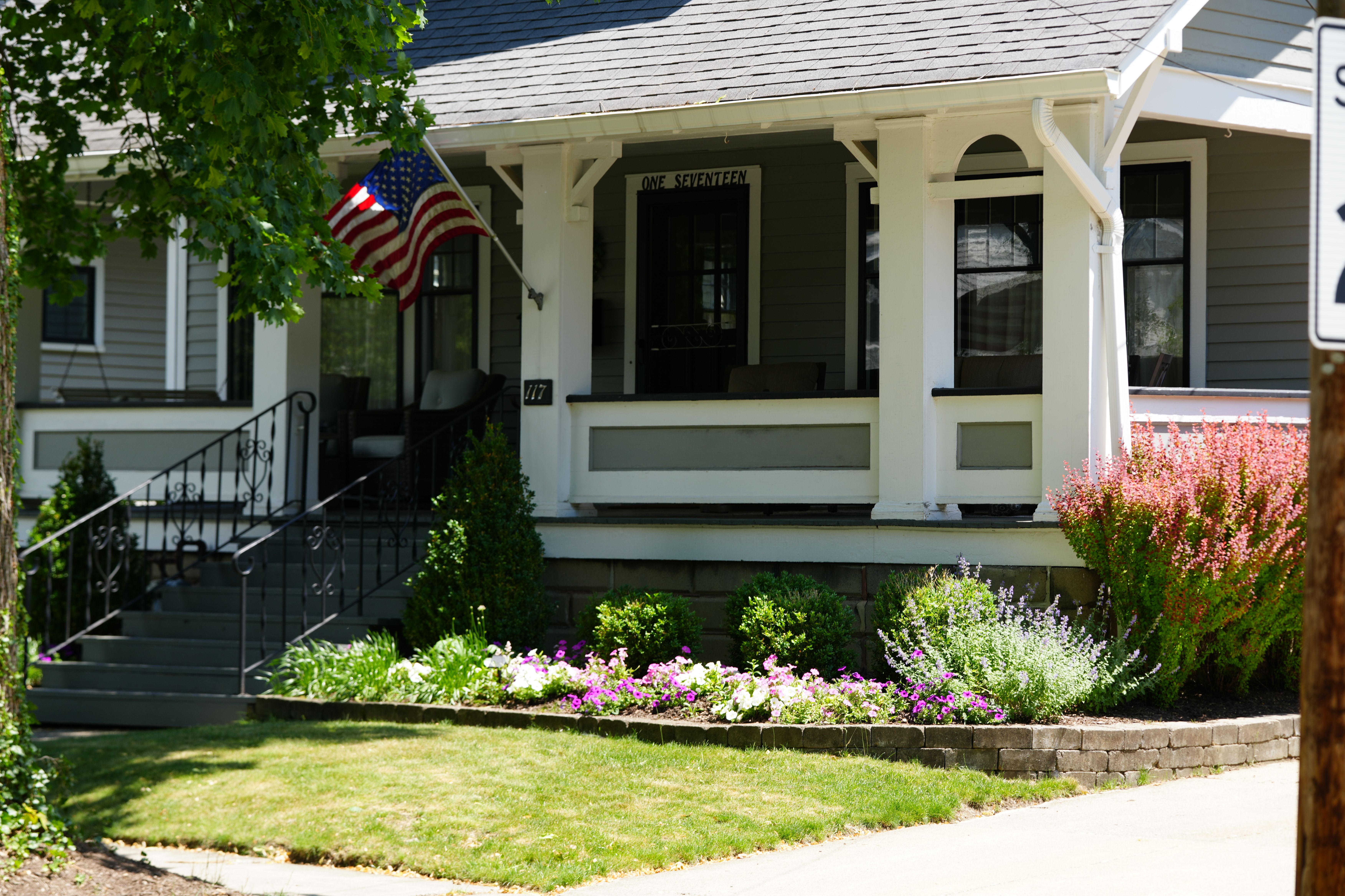 A traditional lawn with a front yard flower bed and american flag.
