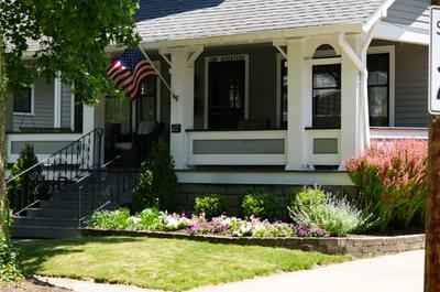 A traditional lawn with a front yard flower bed and american flag.
