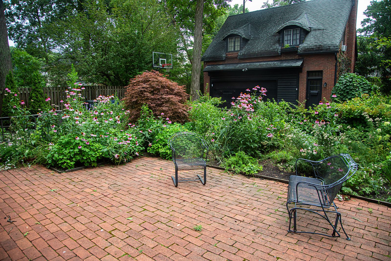 Brick base patio with metal deck chairs in front of a large native, green garden at someones home