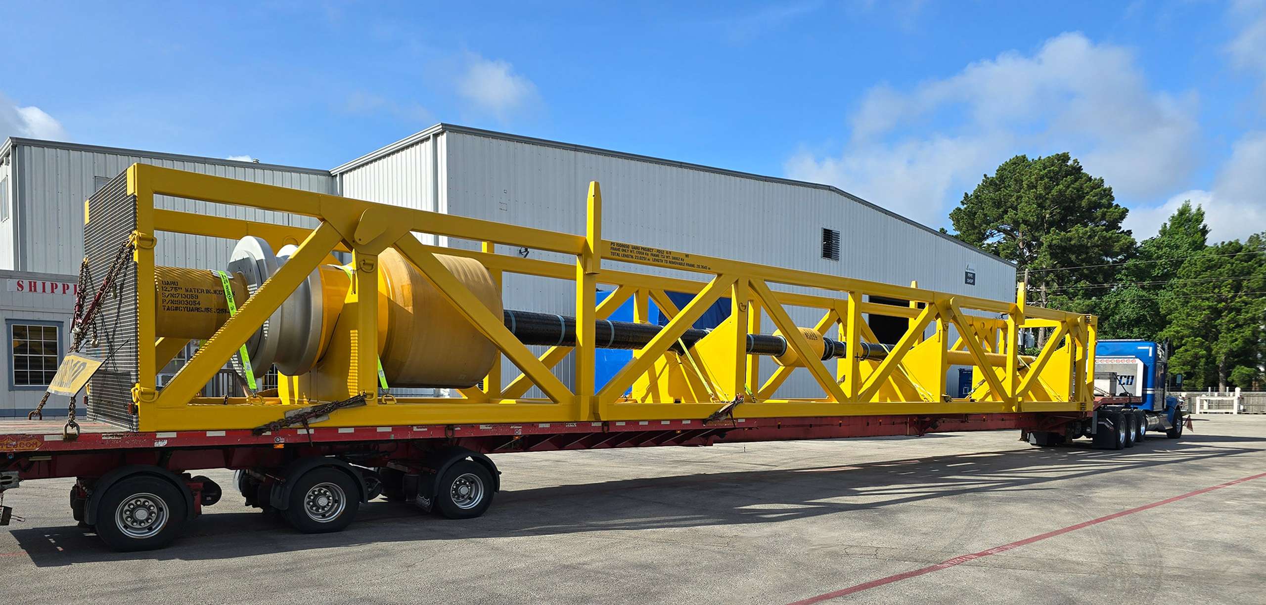 truck carrying long yellow metal structure in industrial yard