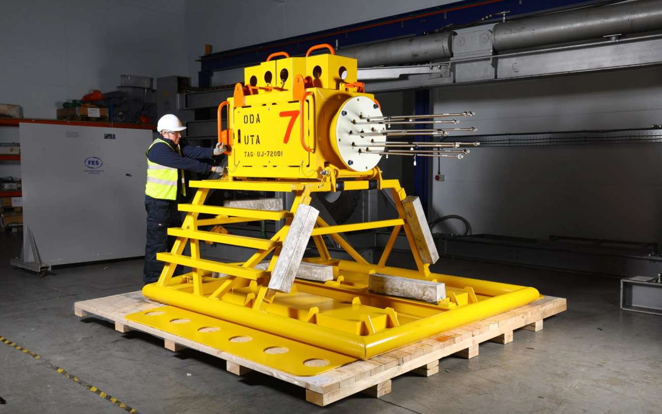 Man in a warehouse inspecting a piece of yellow subsea equipment