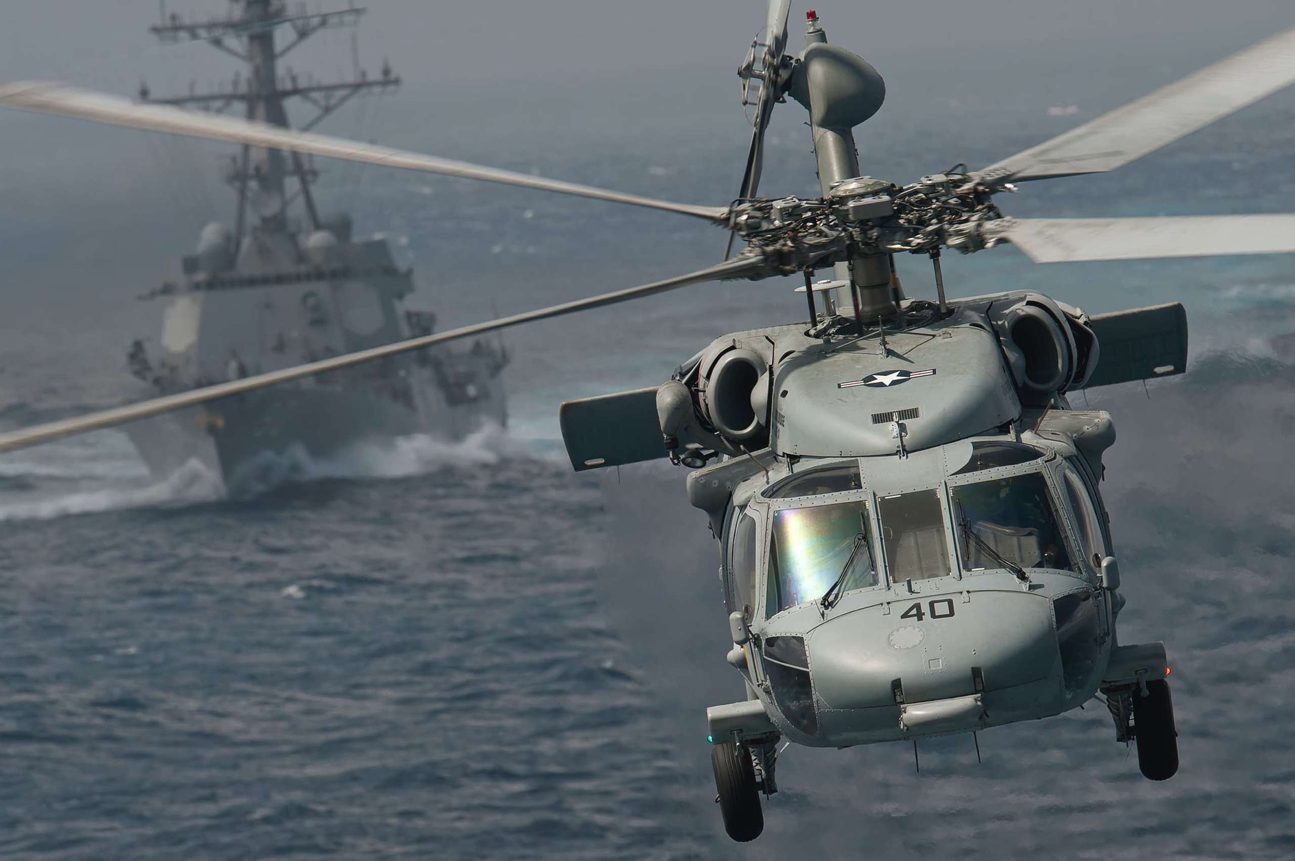 Helicopter flying towards camera with war ship in background