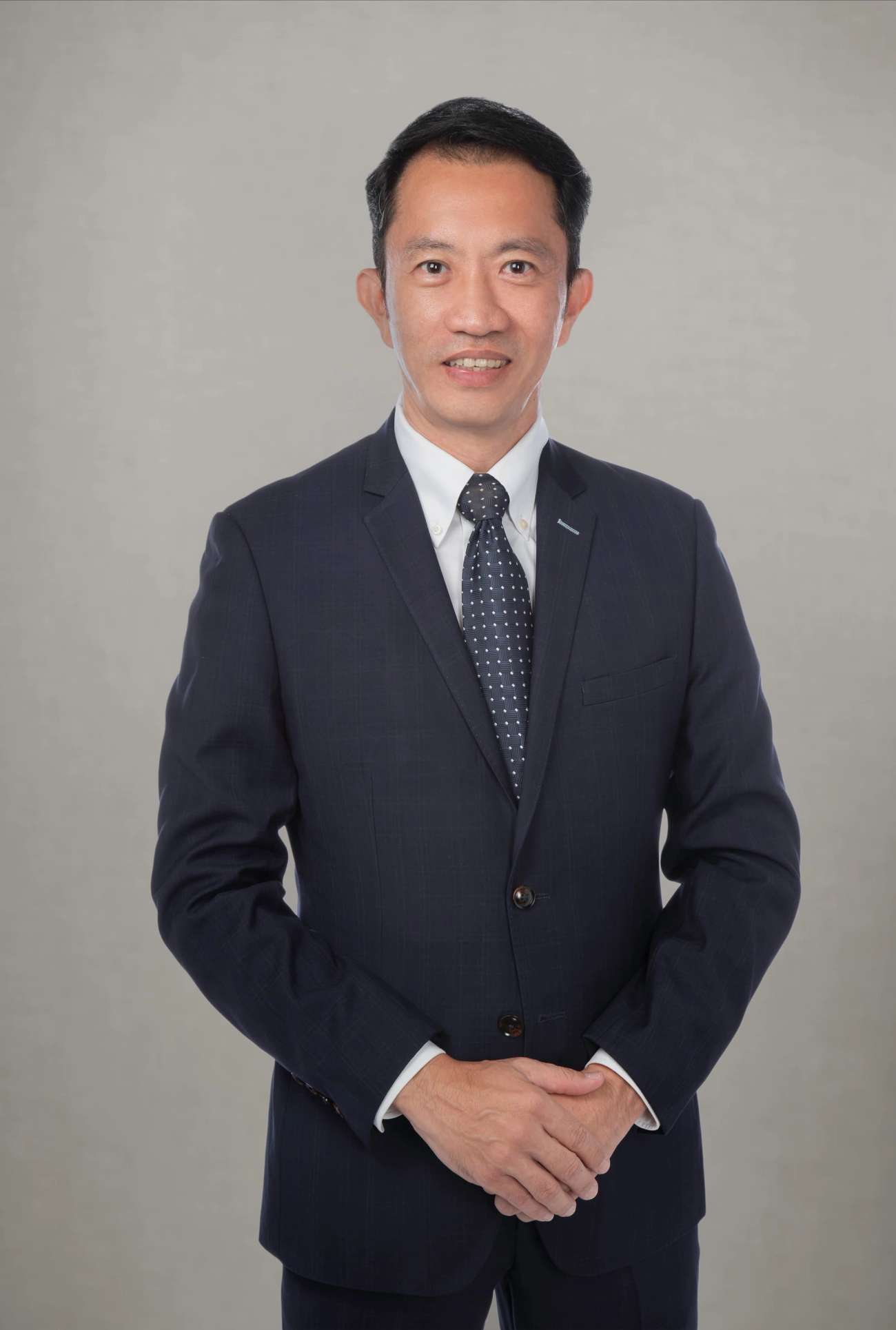 Man with short black hair in navy suit both hands in front of his body