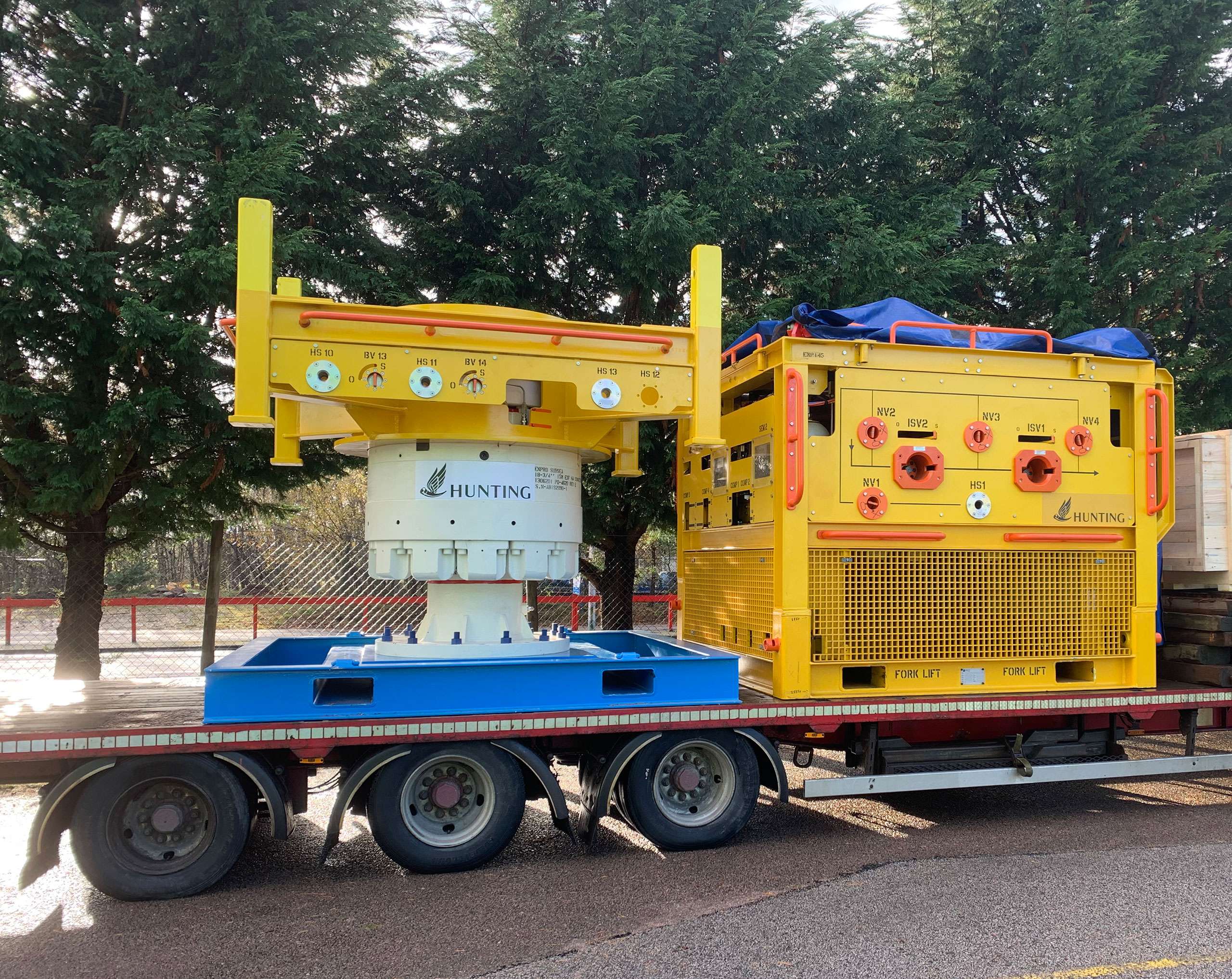 Yellow subsea equipment on back of a trailer on a road with trees in background