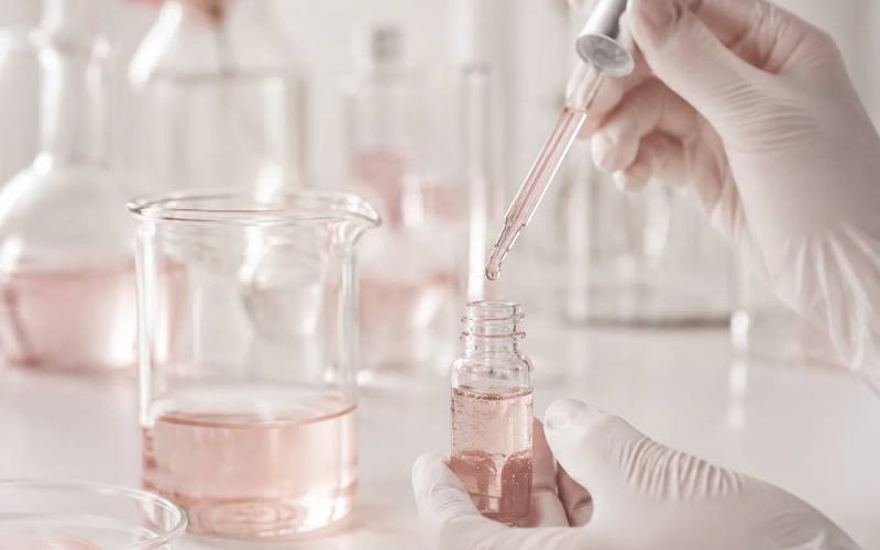 A gloved hand pipetting a sample into a small bottle on a formulation bench