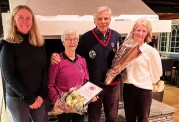 Tre damer og en mann står forann en hvit peis. En dame og en mann har hver sin blomsterbukket og diplom