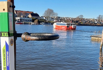 Stolpe festet på jernstang forann elven der en rød ferge kjører