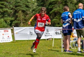 Gutt løper i FSK-drakt med bannere i bakgrunnen