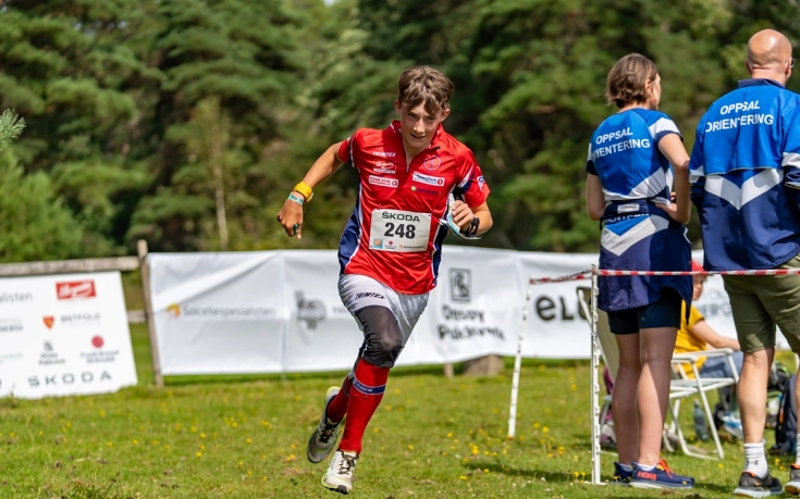 Gutt løper i FSK-drakt med bannere i bakgrunnen