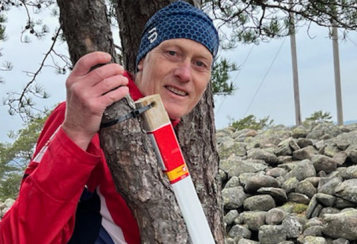 Mann står ved tre og holder en stolpe