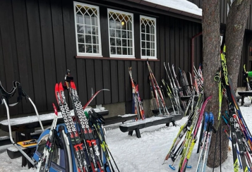 Mange par ski står utenfor en tømmerhytte