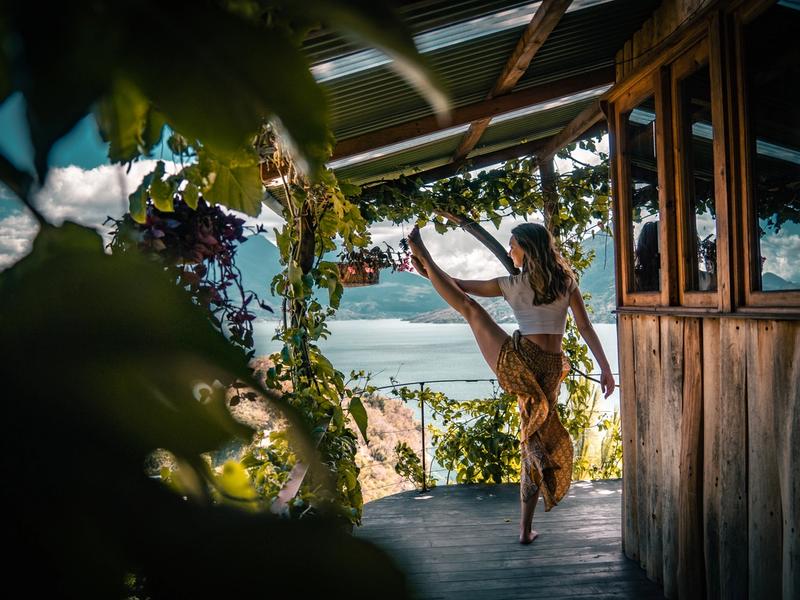 Frau, die auf einer Plattform mit Blick auf den Atitlán-See eine Yoga-Pose im Tanzstil ausführt