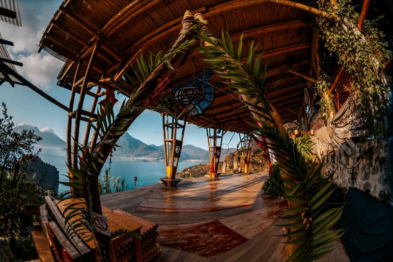 Community yoga platform framed by palm fronds with Lake Atitlan and three volcanoes