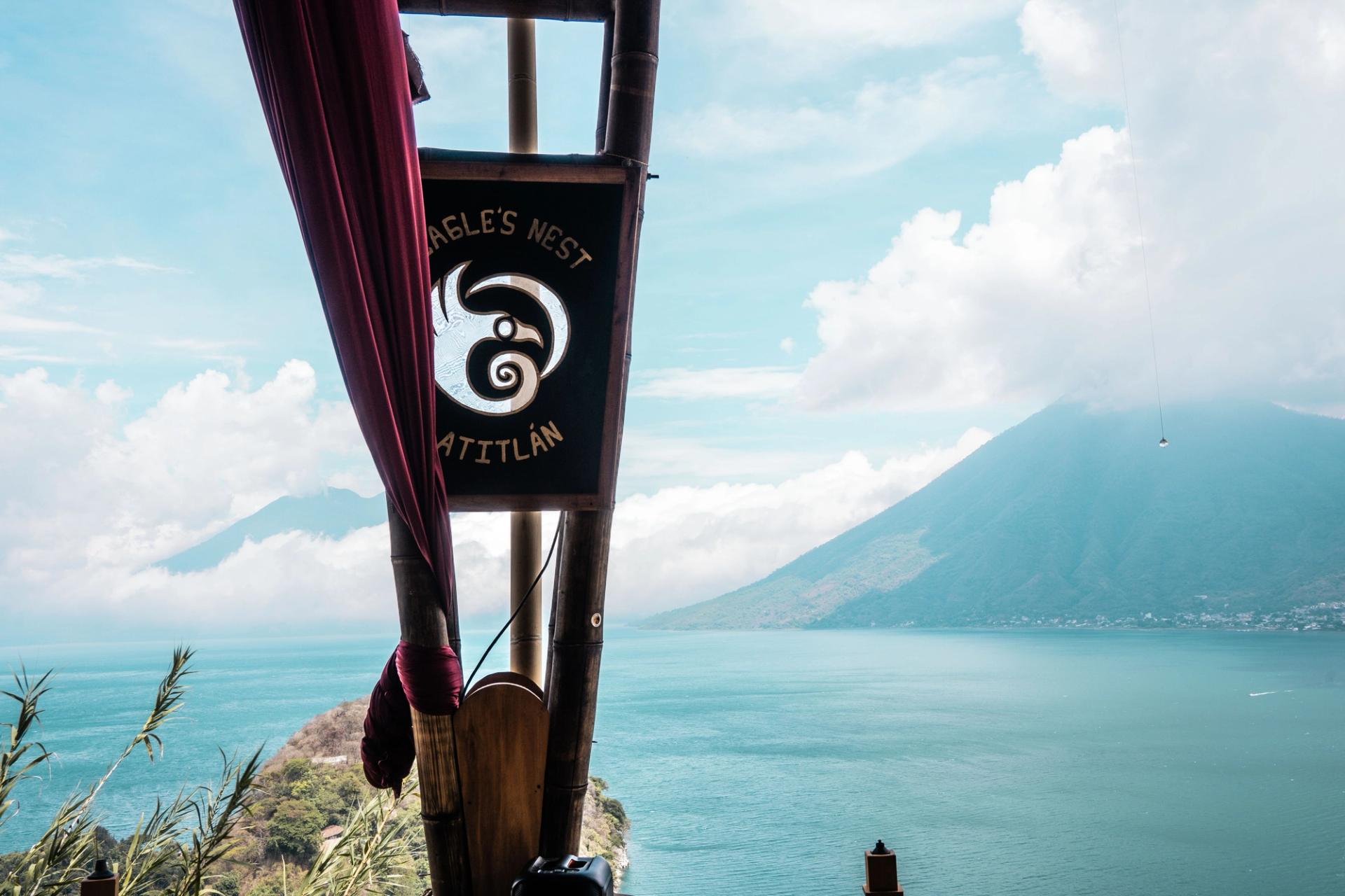 Eagle's Nest Atitlan sign in a bamboo frame on the hillside above San Marcos La Laguna, looking out over Lake Atitlan to a volcano