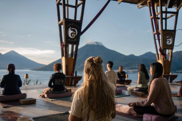 Guests meditating on cushions on the Eagle's Nest yoga platform, facing Lake Atitlan and its volcanoes