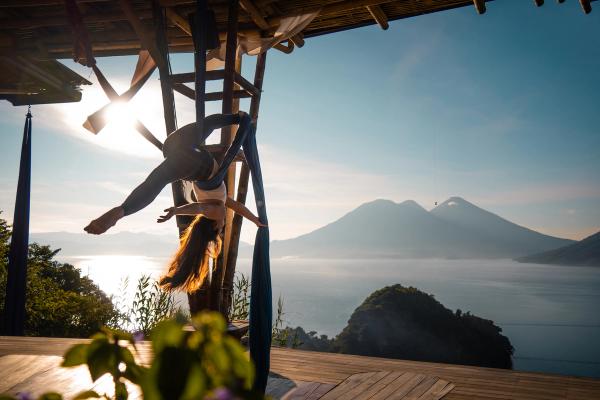 Aerial silks artist inverted against sunrise with volcano backdrop