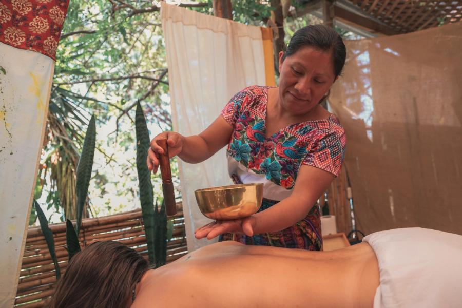 Therapeut, der eine Klangschale über einem mit einem Tuch bedeckten Massageklienten im Behandlungsraum im Garten hält